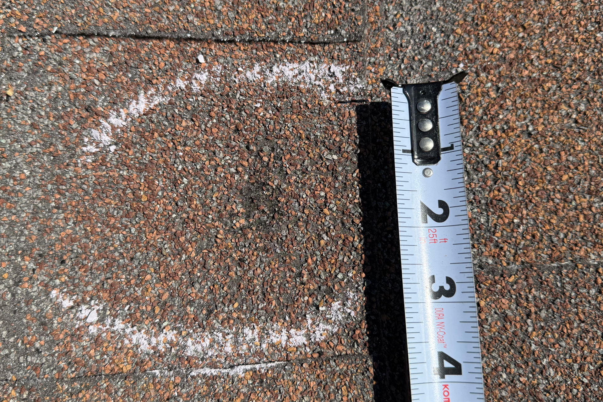 A close-up of a shingle roof shows a white chalk circle marking a spot, with a measuring tape next to it indicating the circle is about 3 inches wide.