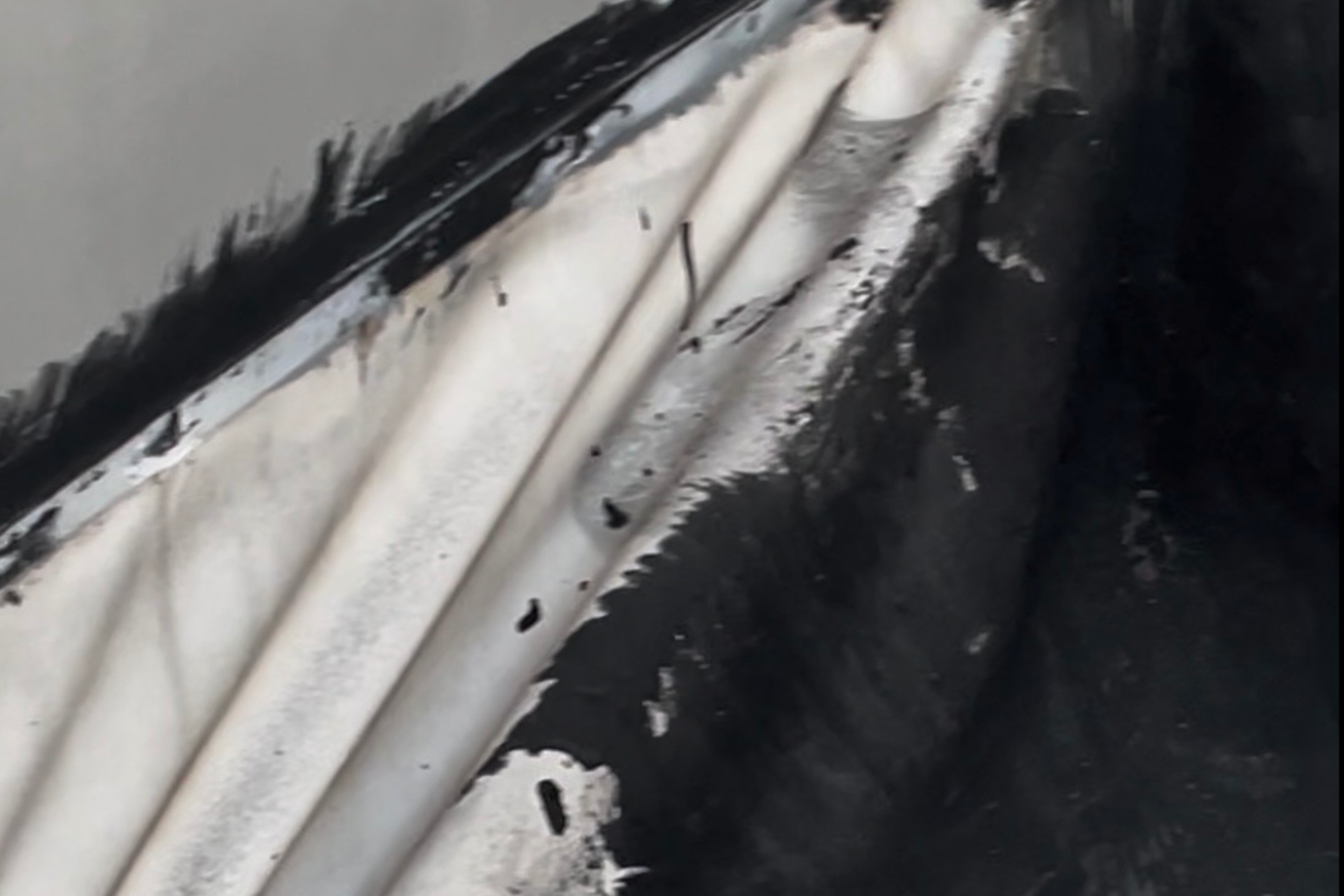 A close-up of a worn, painted metal surface with peeling white paint and black areas, creating an abstract pattern of light and dark patches.